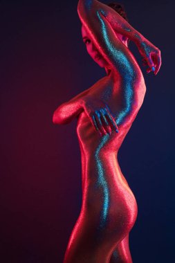 Neon ışıkta poz veren altın kaplamalı seksi kız.