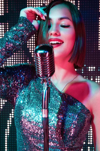 Neon ışıklı güzel kız karaoke 'de şarkı söylüyor. Elinde bir mikrofon var.