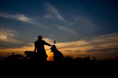 Bir motosiklet üzerinde oturan bir adam silüeti. Günbatımı