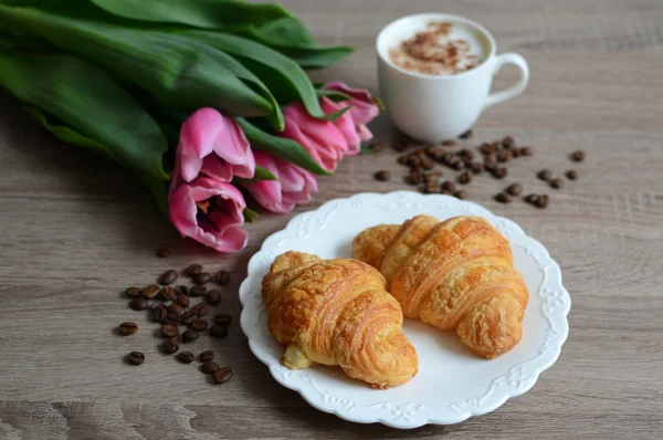 Cup of coffee and yummy croissant with flowers — Stock Photo, Image