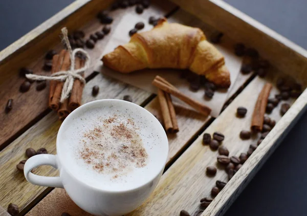 Cup of cappuccino and croissant on the wooden tray