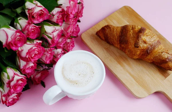 Kopp cappuccino och smaskiga croissant med rosa rosor — Stockfoto