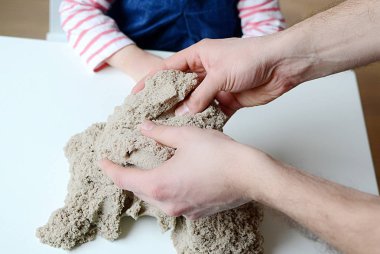 Kız bebek Kinetik kumla oynamak. Babasının ellerini