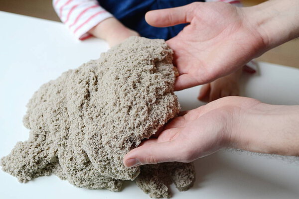 Baby girl play with kinetic sand. Father's hands