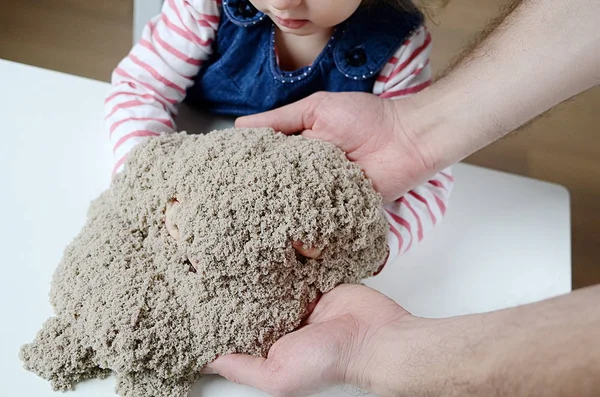 A menina brinca com areia cinética. As mãos do pai — Fotografia de Stock