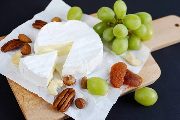 Бри сыр с орехами, сухофрукты и зеленый виноград в деревянной тарелке — стоковое фото