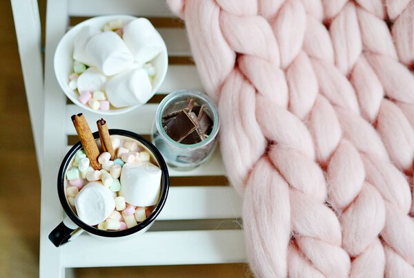 Чашка с горячим шоколадом, миска с зефиром, банка с шоколадом, розовый пастельный гигантский клетчатый, белый стул, утренняя концепция
