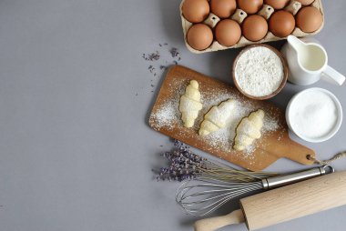 Malzemeler kruvasan yemek pişirmek için pişirme. Hamur, yumurta, beyaz şeker, un, süt, yağ tereyağı. Hazırlık, lavanta çiçekleri. Masa mutfak mutfağı gri arka plan, ev yapımı