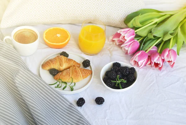 Breakfast in bed, croissant, coffee cup, berries, orange juice, pink tulips, flowers in romantic style, wooden tray
