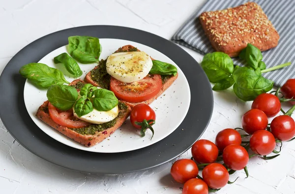 Sandwich with pesto, mozzarella cheese and red tomatoes, basil leaves, pepper, olive oil, gray plate, healthy breakfast, food concept, white background