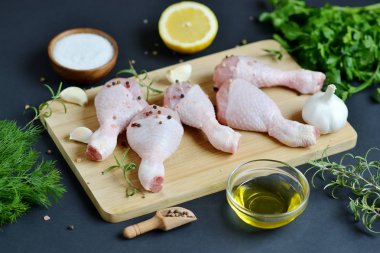 Yeşil otlar ve baharatlar biber ahşap kesme tahtası gıda içerikler tuz biberiye limon yağı hazırlık yaşam tarzı sağlıklı kavramı siyah arka plan üzerinde çiğ tavuk budu