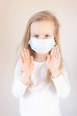 Beyaz bir arka planda yüzünde tıbbi maske olan küçük sarışın kız. Koronavirüs korunuyor.