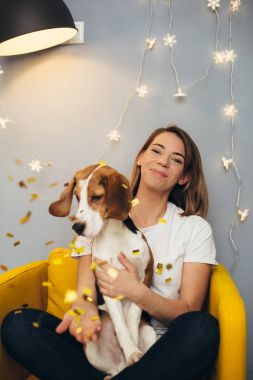 Beagle yavru ve konfeti sarı sandalye ile gri duvar ve zemin lambası arka plan üzerinde beyaz t-shirt genç kadın
