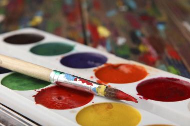 Kırmızı boya yalanlar üzerine suluboya boya kümesi içinde bir fırça boyalı. Yakın çekim. Netlik üzerinde fırça ucu.