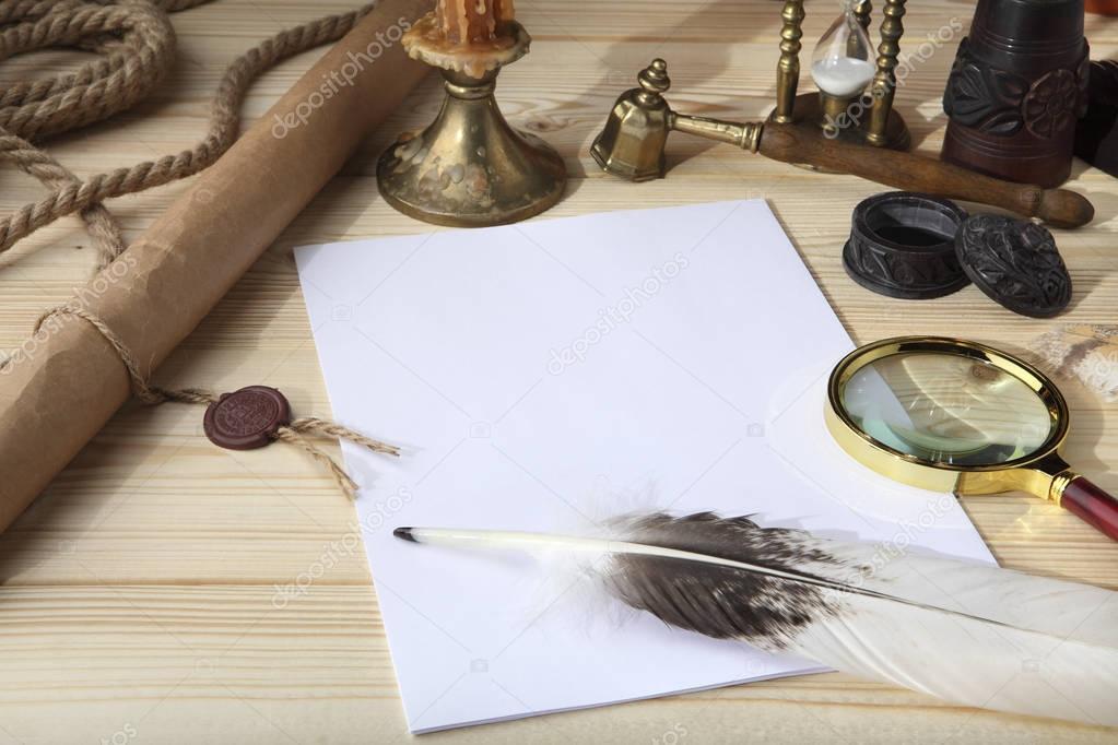 A pile of clean paper, a retro inkwell with black ink, a goose feather, magnifying glass, a scroll with a seal, an old hourglass and a bronze candlestick on a wooden table. Retro stylized photo