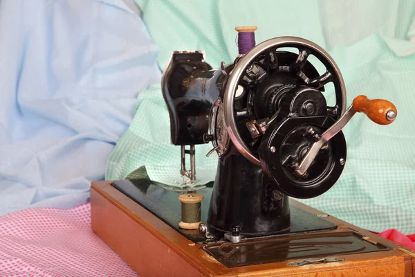 Vieja máquina de coser a mano con una aguja, bobinas retro de hilos de colores y piezas de tela de algodón de color. Antecedentes para su diseño. La máquina de coser es girada por el mango a la viewe — Foto de Stock