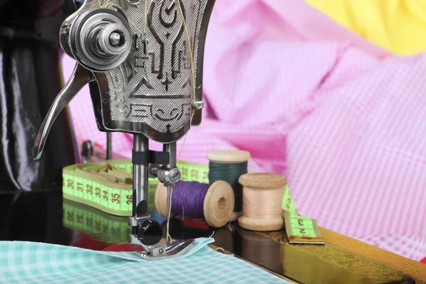 Auf der alten Nähmaschine liegen hölzerne Retrospulen mit Fäden, einem Fingerhut, einem Maßband und einem Stück Baumwollstoff. Nahaufnahme. Retro stilisiertes Foto. — Stockfoto