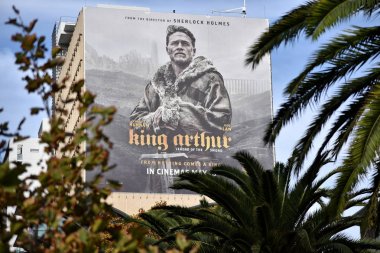 Perth, Australia - May 30, 2017: View of King Arthur billboard poster framed by foliage seen on city center building. clipart