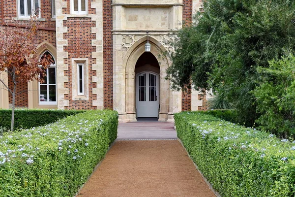 Big vintage house exterior with brown and brick facade, grey door and tidy bushes with trees