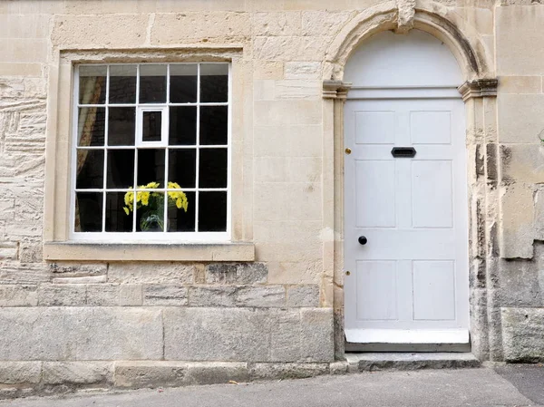 View of old classical house with stone facade, tidy white door, window and yellow flowers on window sill