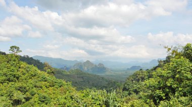 Dağ doruklarına zengin bitki örtüsü, bulutlar ve mavi gökyüzü ile