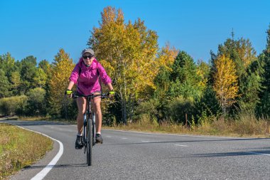 Kız bir bisiklet ile sonbahar bir yolda gidiyor