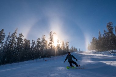 Snowboard slaytlar güneş halo arka plan ile karlı tepe aşağı