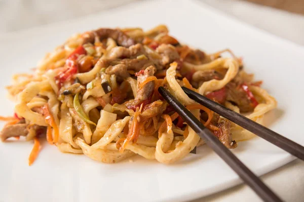 Egg udon noodles with pork, vegetables and sesame seeds on a white plate, hinese chopsticks — Stock Photo, Image