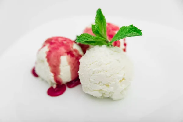 Три ложки морозива з полуничним сиропом і м'ятою на білій тарілці, білий фон — стокове фото