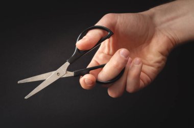 Küçük bir çift makas tutan erkek el. Fotoğraf el siyah bir zemin üzerine