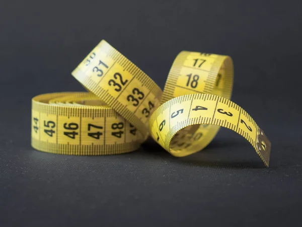 Yellow tape measure on rolled up on black background