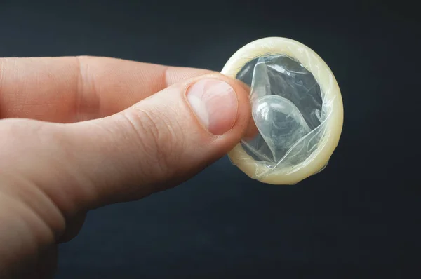 Preservativo na mão masculina sobre fundo preto — Fotografia de Stock