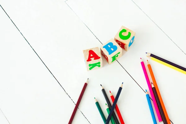 wooden english abc cubes and colorful pencils on the white neutr