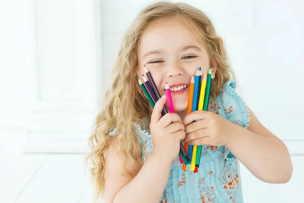 Malá holčička s úsměvem do kamery s barevné tužky v jejích rukou — Stock fotografie