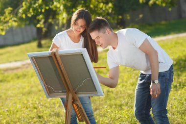 Genç çift, şövale çizerek renkli alacalı boyalar. Öncesi