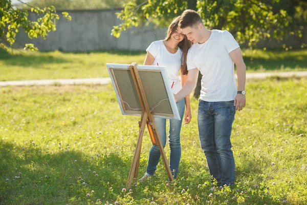 Young couple drawing at easel by colorful variegated paints. Pre