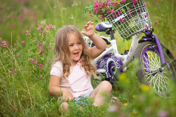 Küçük şirin kız Bisiklet l yakınındaki çiçek alan dinlenme — Stok fotoğraf