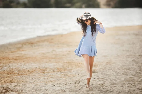 Young woman in big striped hat walking on sandy beach