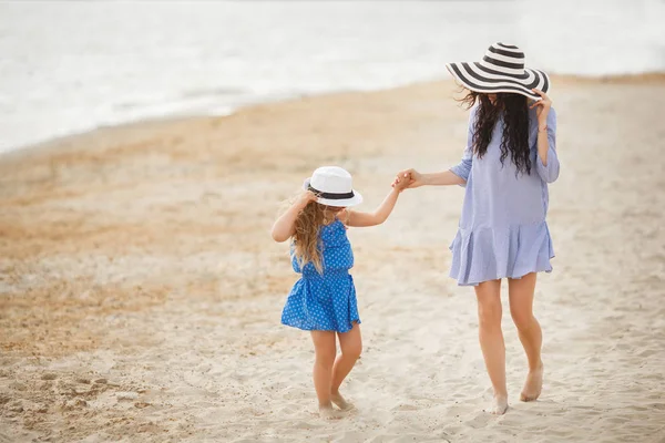 小さな娘と砂浜の上を歩いて楽しんでストライプ帽子の母 — ストック写真