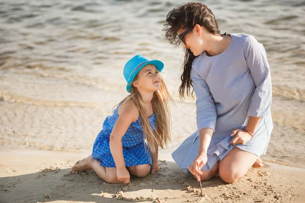 Mother with daughter drawing on sand near water