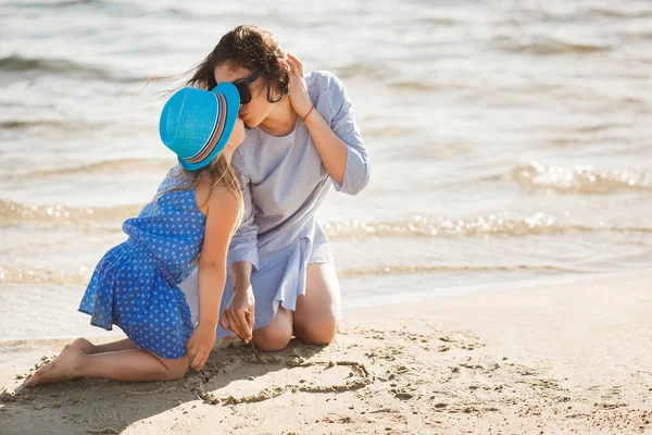 Mother with daughter drawing on sand near water