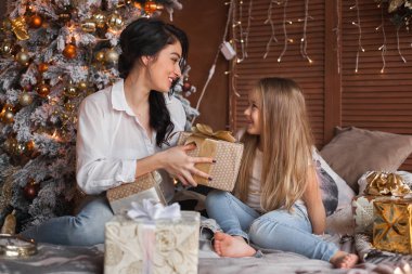 Genç anne ve kızı yatakta Noel hediyeleri açma