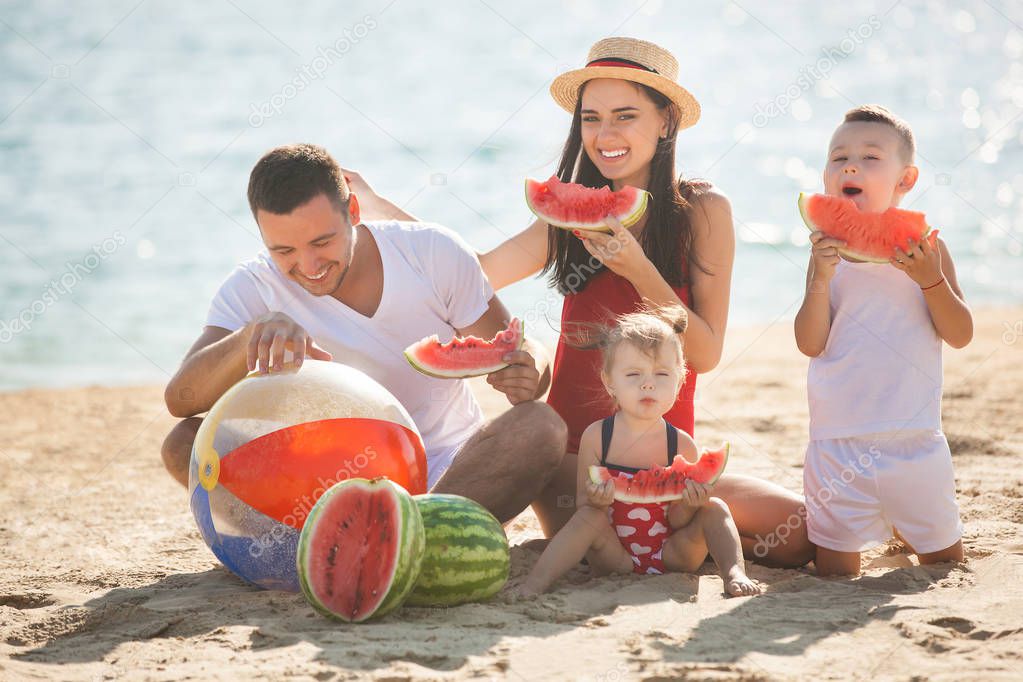 Young parents with children eating watermelon on beach