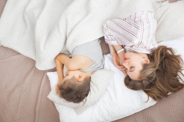 Anne ile oğlu beyaz battaniye altında yatakta yatmak 