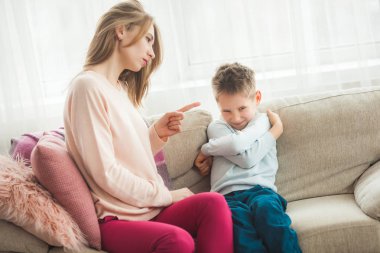 Mother punishing son on couch at home clipart