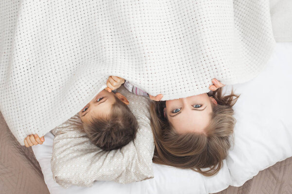 sleepy mother lying in bed with son under white blanket