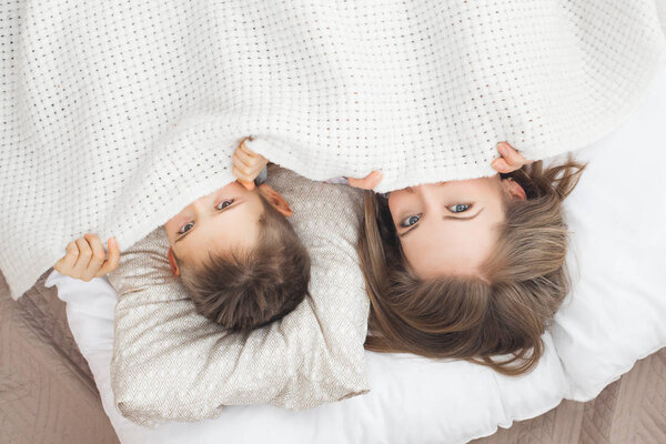 sleepy mother lying in bed with son under white blanket