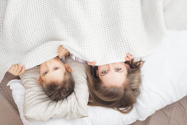 sleepy mother lying in bed with son under white blanket