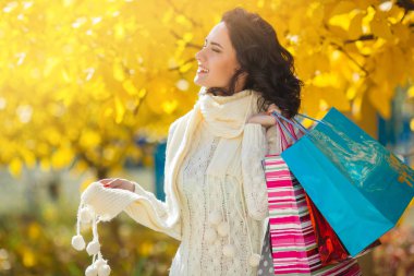 Alışveriş yaparken neşeli genç kadın. Güzel kız alışveriş torbaları ile sonbahar arka plan açık açık havada.