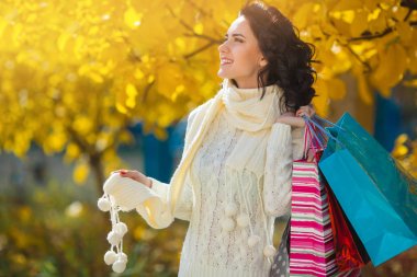 Alışveriş yaparken neşeli genç kadın. Güzel kız alışveriş torbaları ile sonbahar arka plan açık açık havada.
